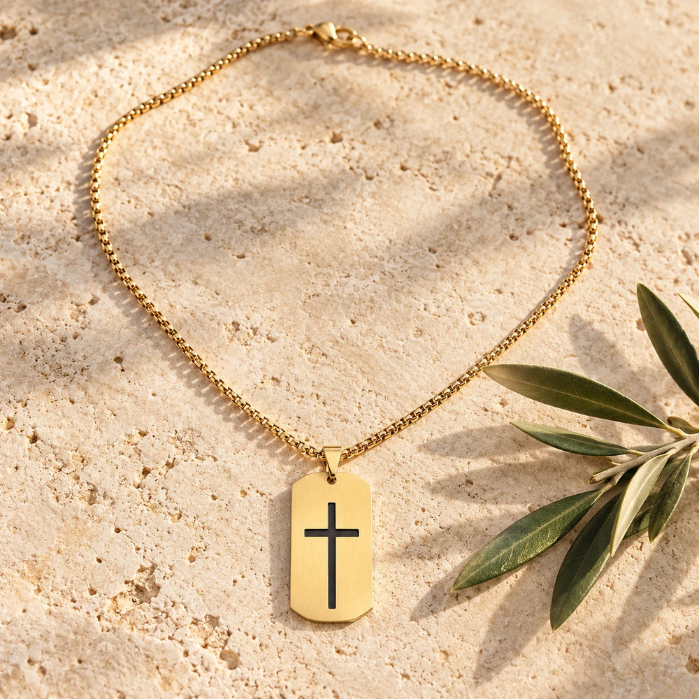 Gold-tone cross tag pendant on a box chain on a pale limestone background, with an olive sprig for scale — true size: the tag is 40 mm tall and 24 mm wide (about 49 mm with the bail), on a box chain about 2.5–3 mm wide