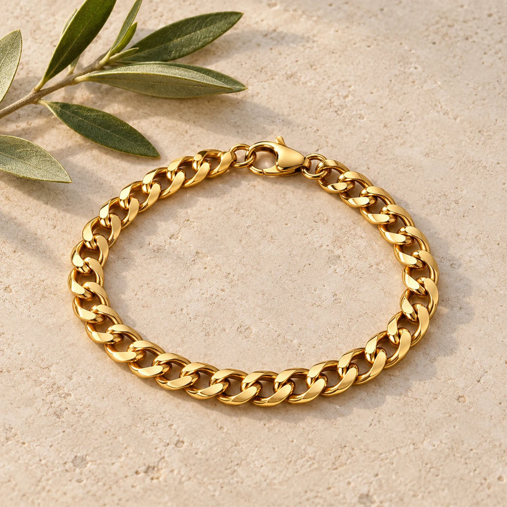 Gold-tone 8 mm cuban chain bracelet on a pale limestone background, with an olive sprig for scale — true size: the flat curb bracelet is 8 mm wide with 2 mm wire, 21 cm long