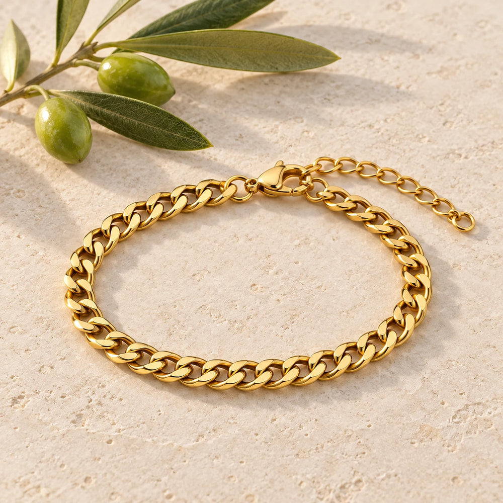 Gold-tone 4 mm cuban chain bracelet on a pale limestone background, with an olive sprig for scale — true size: the flat curb bracelet is 4 mm wide with 1 mm wire, 17 cm + 5 cm extender
