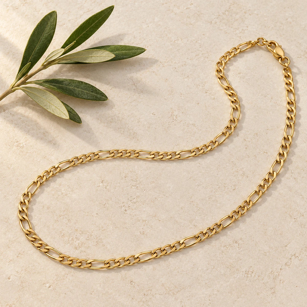 Gold-tone 3 mm figaro chain necklace on a pale limestone background, with an olive sprig for scale — true size: the figaro chain is 3 mm wide with 0.8 mm wire