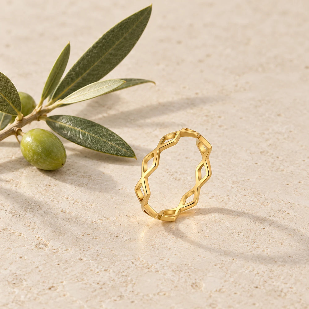 Gold-tone slim ring of crossing waves with diamond-shaped openings on a pale limestone background, with an olive sprig for scale — true size: the band is only 4 mm wide, made of hair-thin wires, with an outer diameter of about 19 mm