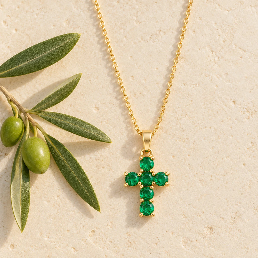Gold-tone cross with six green stones on a fine chain on a pale limestone background