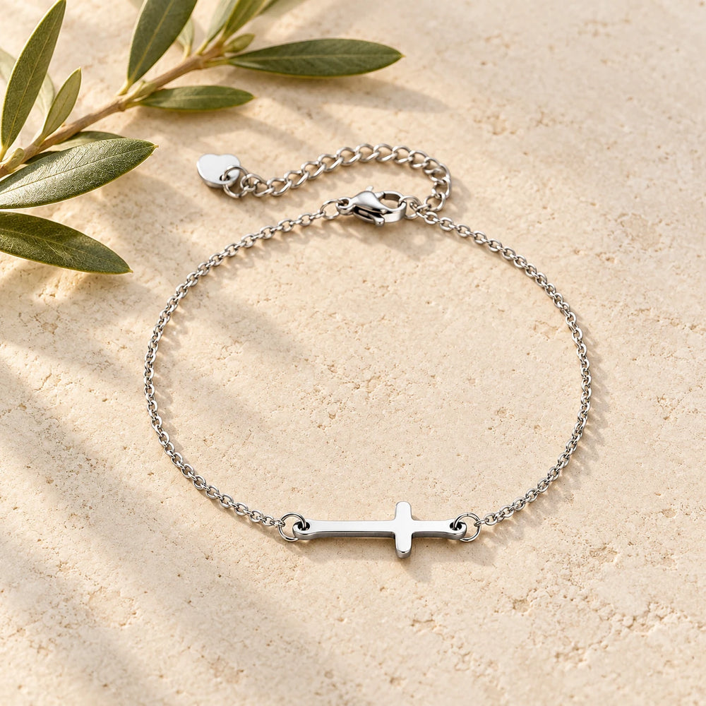Silver-tone fine bracelet with a small sideways cross on a pale limestone background, with an olive sprig for scale — true size: the slim sideways cross is about 21 mm long and 7 mm tall, on a fine cable chain about 1.5 mm wide