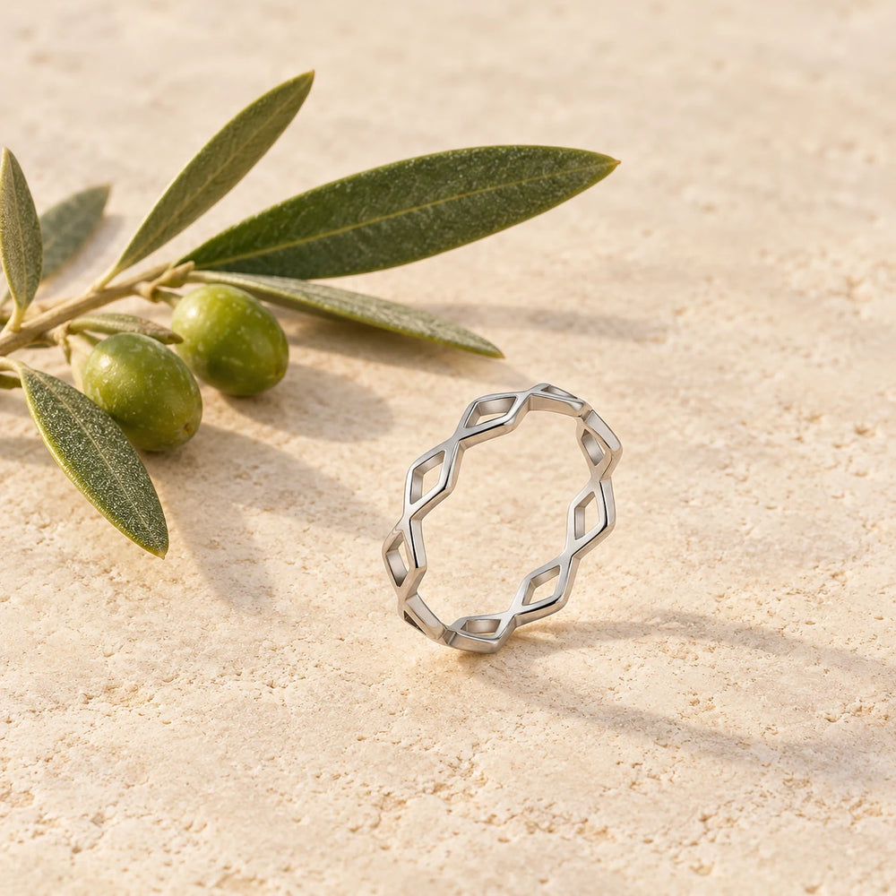 Silver-tone slim ring of crossing waves with diamond-shaped openings on a pale limestone background, with an olive sprig for scale — true size: the band is only 4 mm wide, made of hair-thin wires, with an outer diameter of about 19 mm