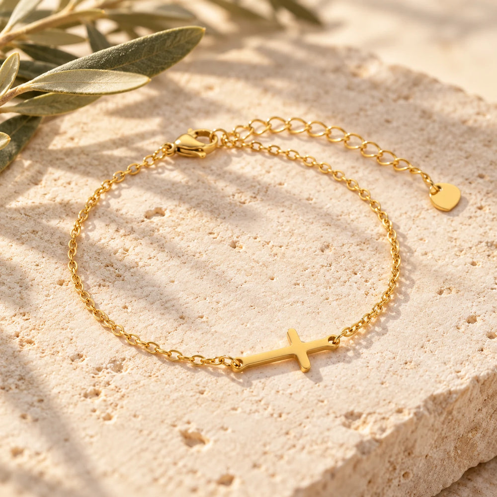 Close-up of the gold-tone sideways cross bracelet on limestone beside olive leaves