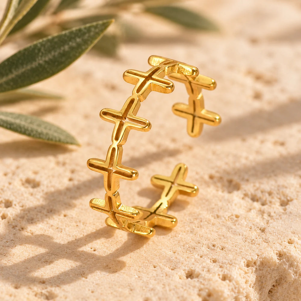 Close-up of the gold-tone band of crosses ring on limestone beside olive leaves