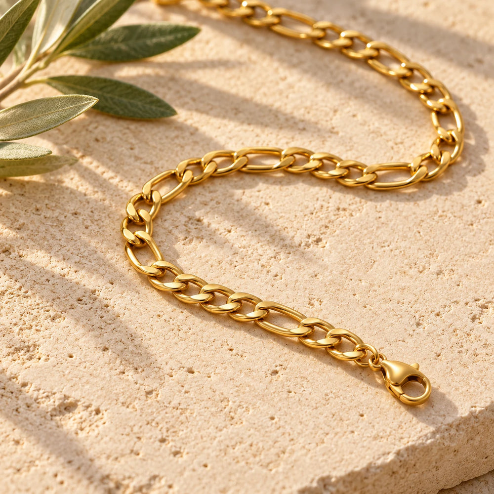Close-up of the gold-tone 5 mm figaro chain necklace on limestone beside olive leaves