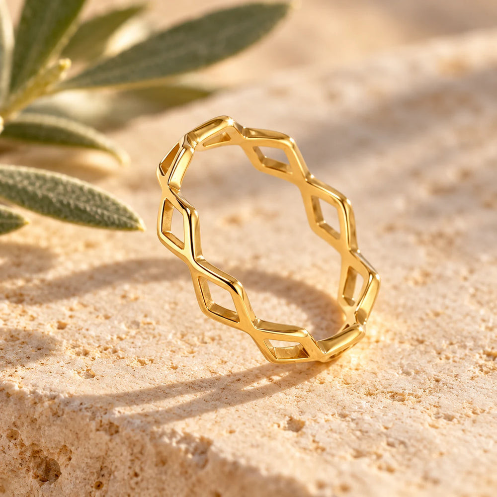 Close-up of the gold-tone woven ring on limestone beside olive leaves