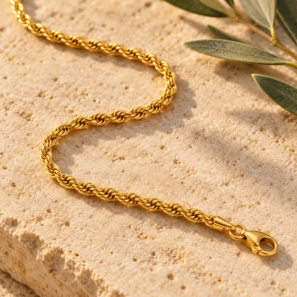 Close-up of the gold-tone 3 mm rope chain necklace on limestone beside olive leaves