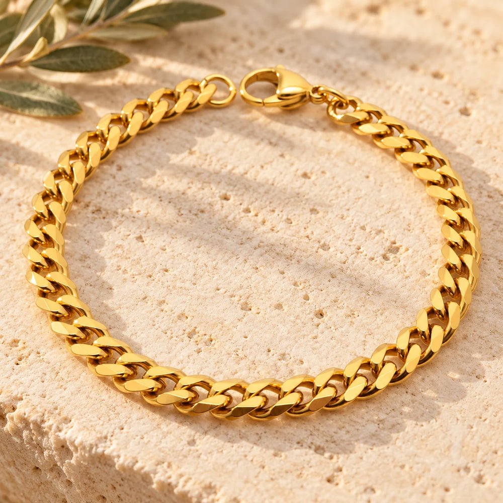Close-up of the gold-tone 6 mm cuban chain bracelet on limestone beside olive leaves