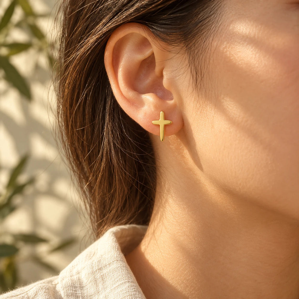 Gold-tone cross stud worn on the earlobe, hair tucked behind the ear
