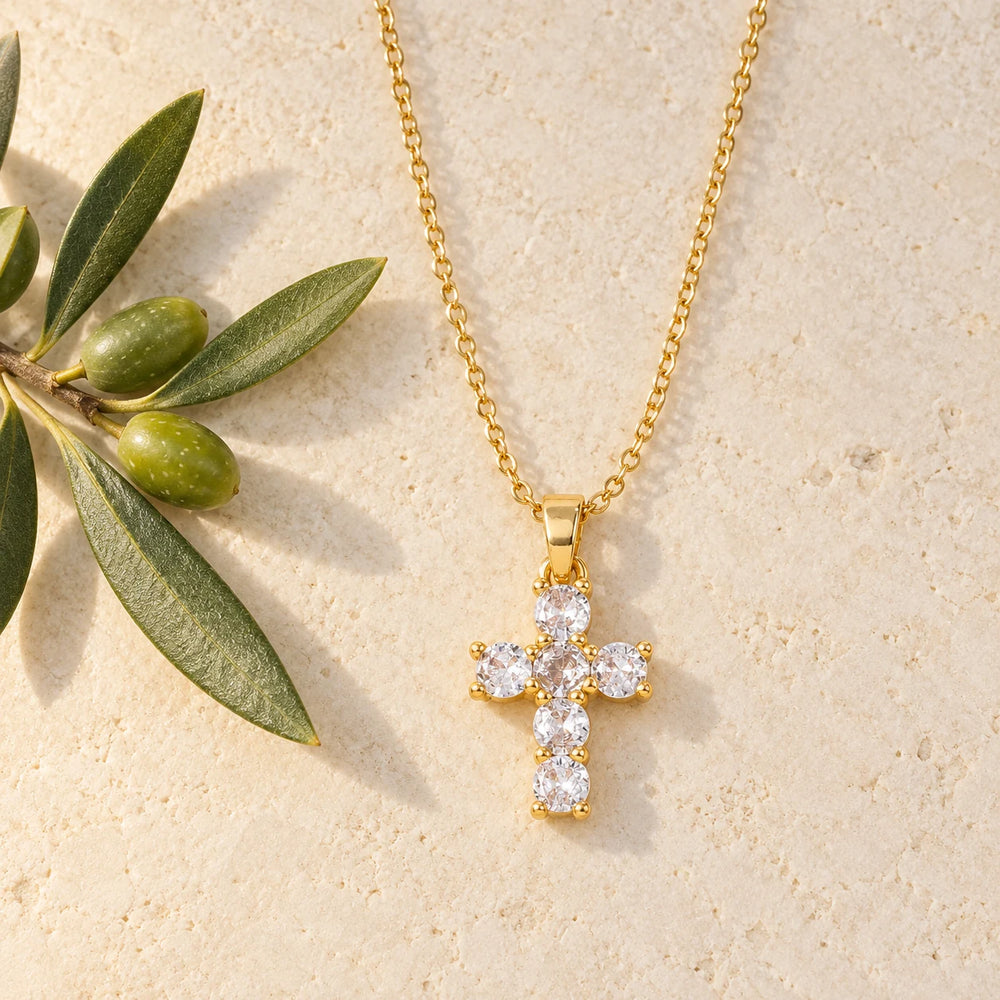 Gold-tone cross with six clear stones on a fine chain on a pale limestone background