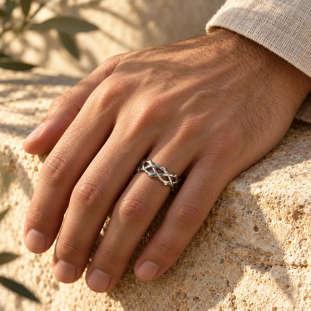 Silver-tone woven crown of thorns ring on a man's hand resting on a limestone wall