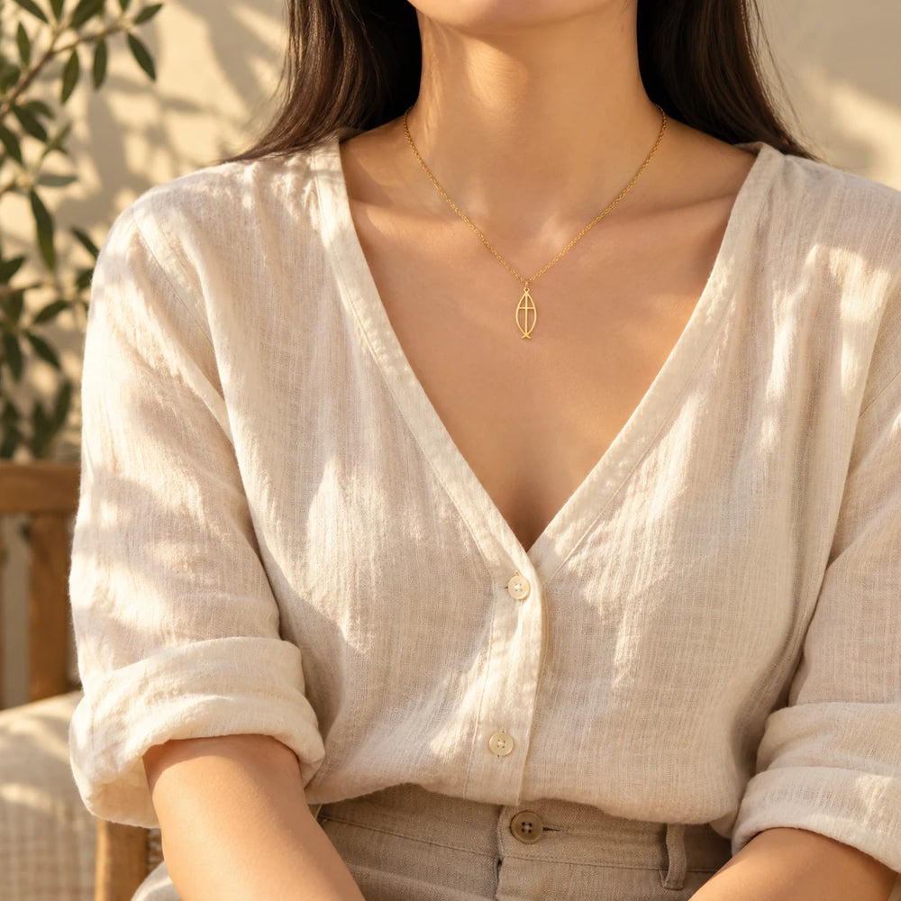 Gold-tone ichthys necklace worn with an oatmeal knit sweater — true size: the open fish pendant is about 23 mm long and 10 mm wide, slim and flat, on a fine cable chain about 1 mm thick