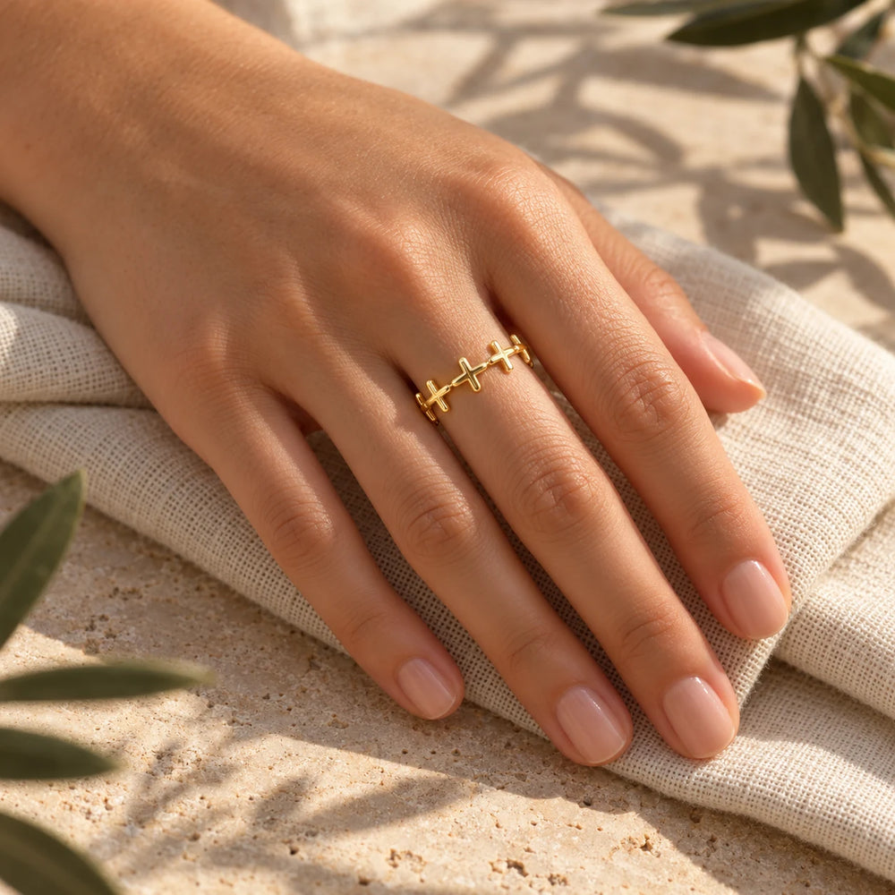 Gold-tone band of crosses ring on a woman's hand resting on folded linen — true size: the band is a single row of tiny crosses 6 mm tall, the ring about 20 mm across