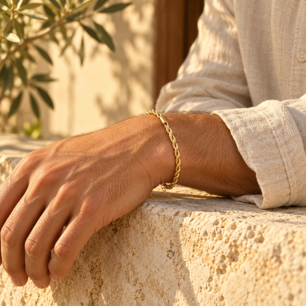 Gold-tone 3 mm rope chain bracelet on a man's wrist resting on a limestone wall