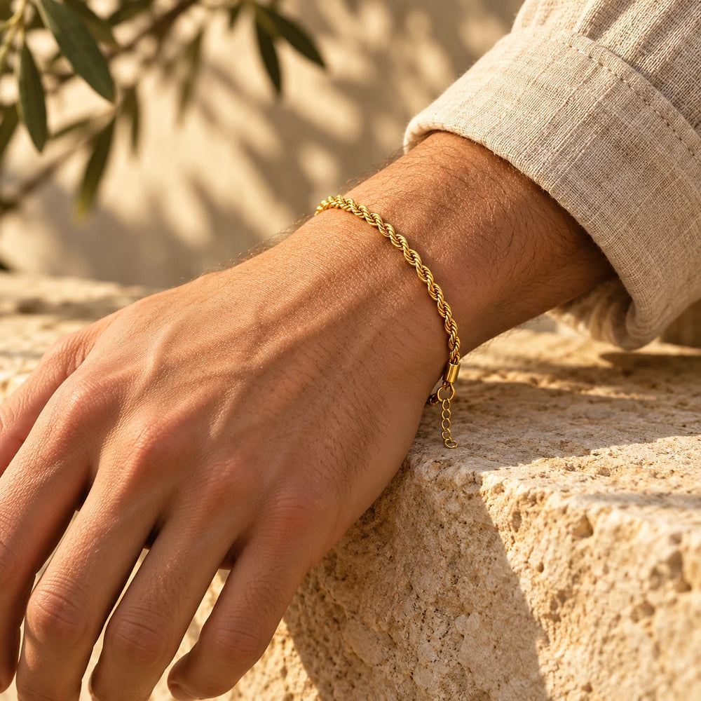 Gold-tone 3 mm rope chain bracelet on a man's wrist resting on a limestone wall — true size: the twisted rope bracelet is 3 mm thick, 17 cm + 5 cm extender
