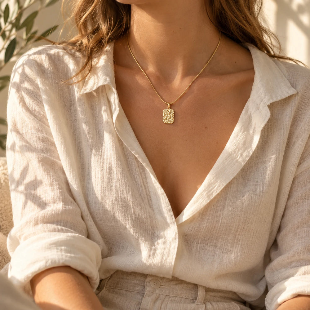 Silver-tone stone-relief tag pendant worn over a cream knit sweater — true size: the square textured tag is 22 mm tall and 16 mm wide (about 28 mm with the bail), on a fine chain about 1.5 mm thick
