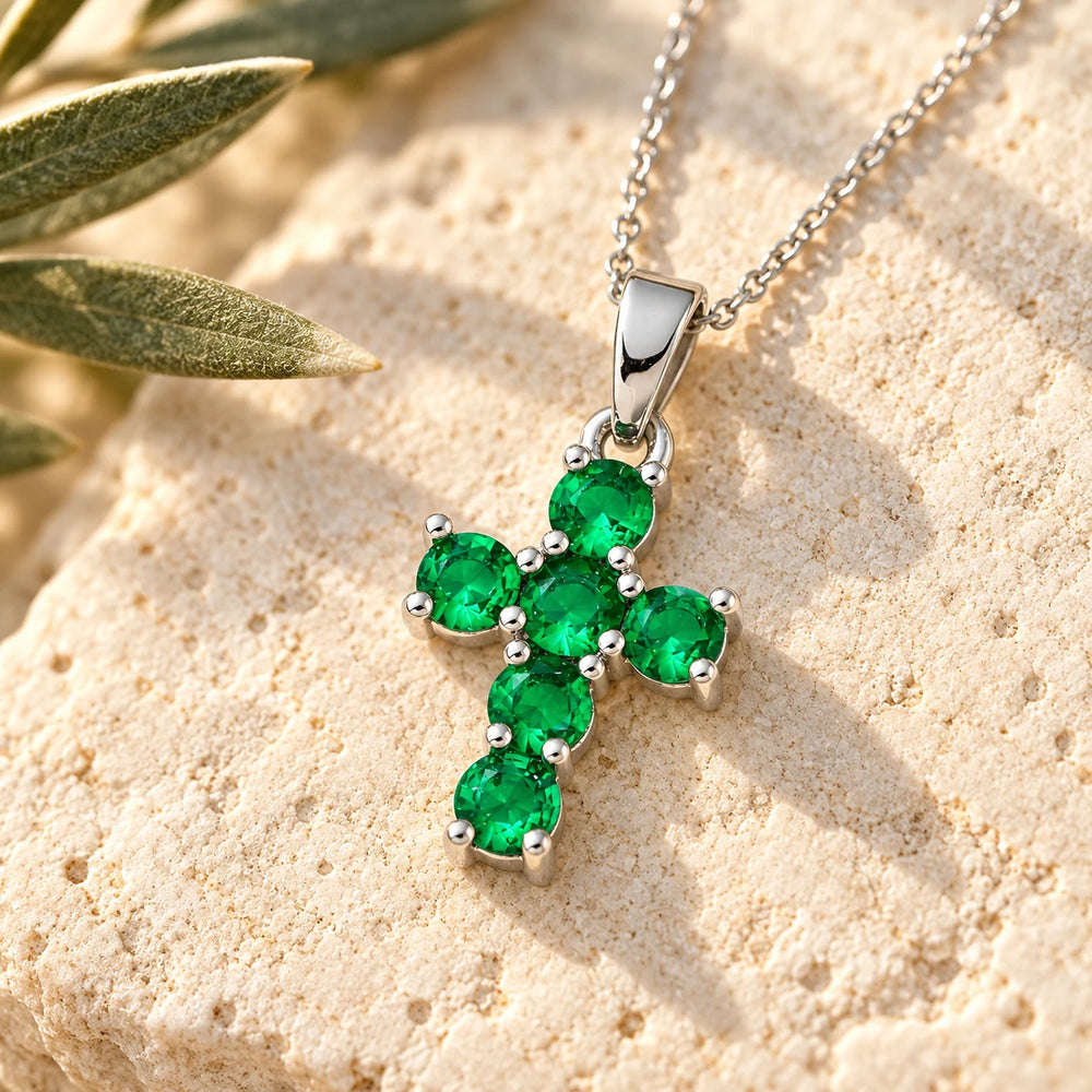 Close-up of the silver-tone cross with six green stones on limestone beside olive leaves