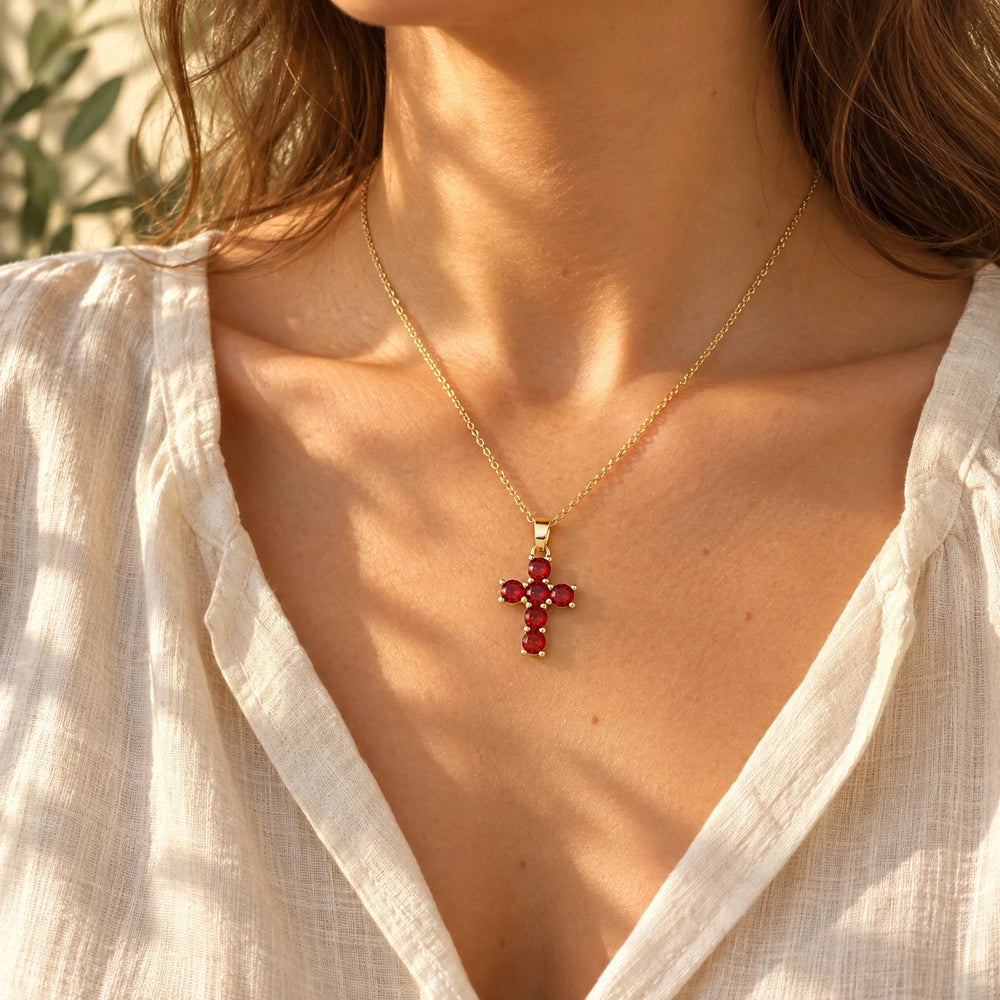 Gold-tone cross with six red stones worn at the collarbone with a cream linen top