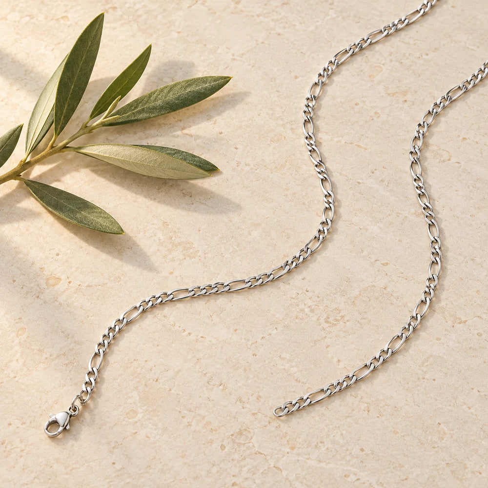 Silver-tone 3 mm figaro chain necklace on a pale limestone background, with an olive sprig for scale — true size: the figaro chain is 3 mm wide with 0.8 mm wire