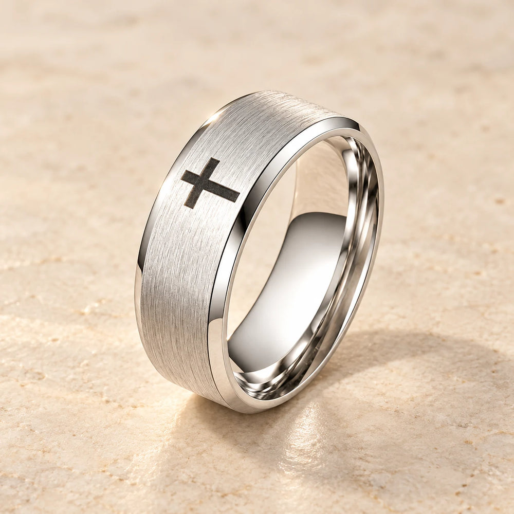 Silver-tone brushed band ring with a small black cross on a pale limestone background