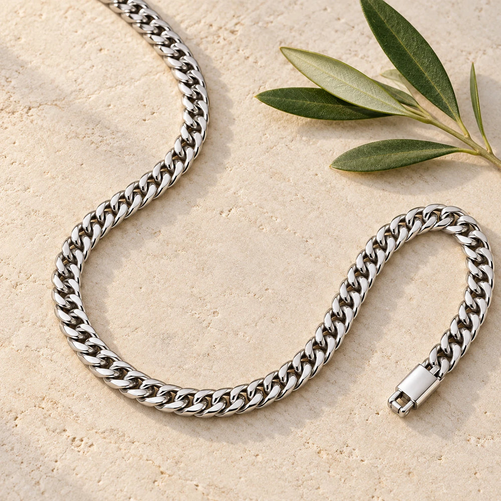 Silver-tone 6 mm cuban chain necklace on a pale limestone background, with an olive sprig for scale — true size: the dense cuban chain is 6 mm wide