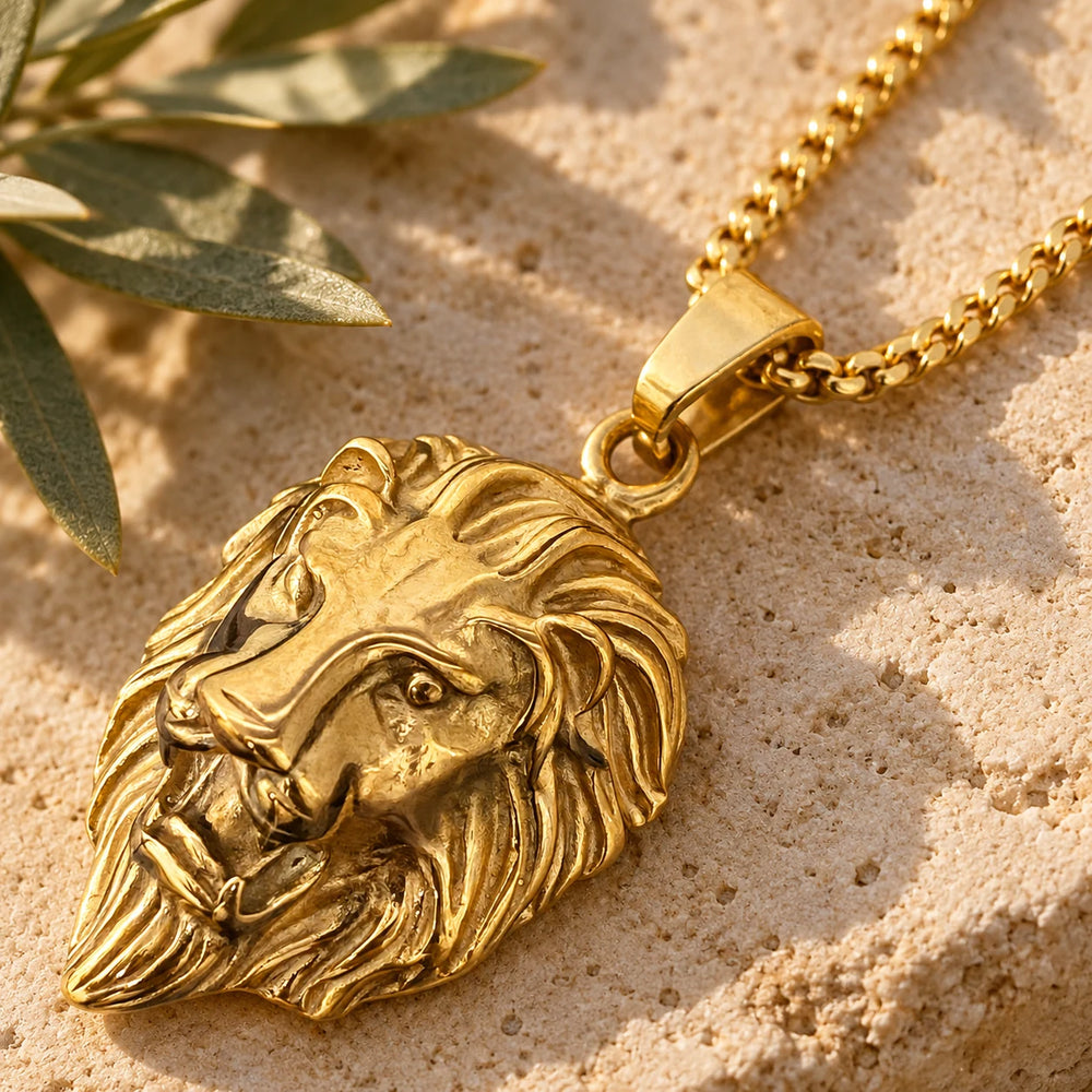 Close-up of the gold-tone lion head pendant on limestone beside olive leaves
