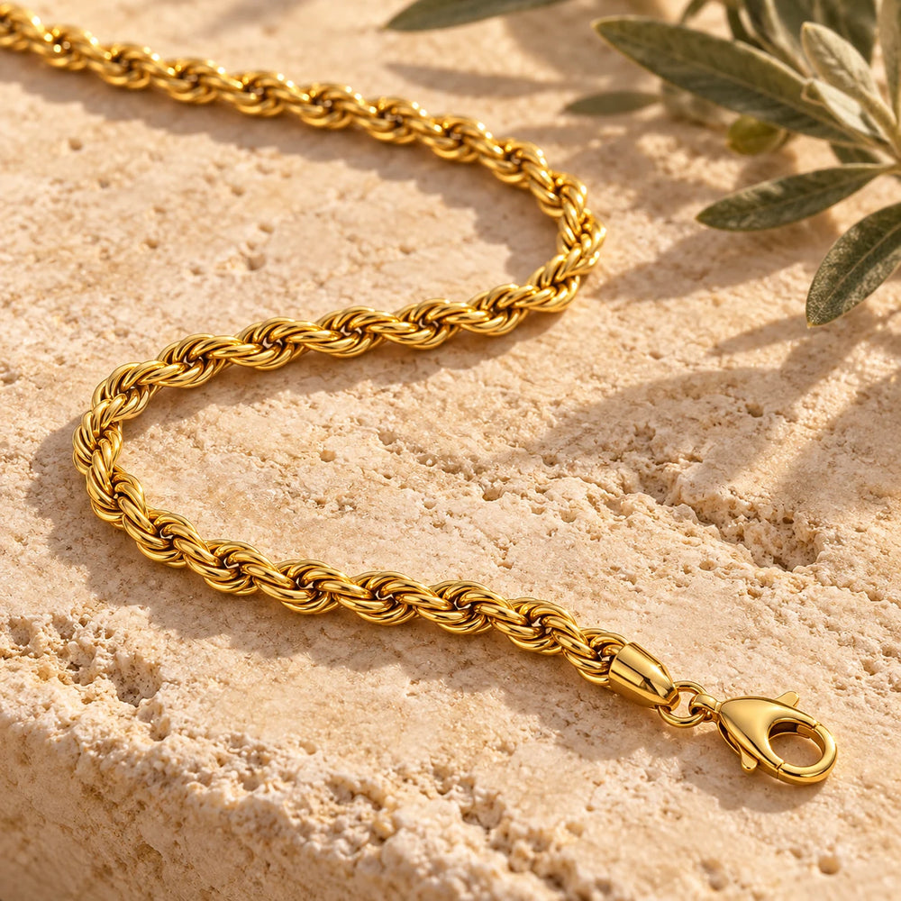 Close-up of the gold-tone 5 mm rope chain necklace on limestone beside olive leaves