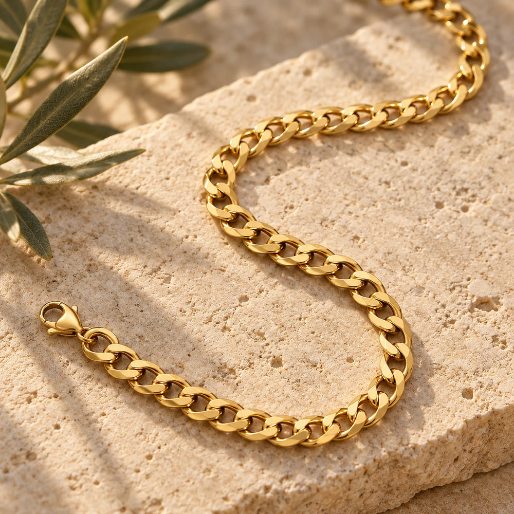 Close-up of the gold-tone 4 mm flat curb chain necklace on limestone beside olive leaves