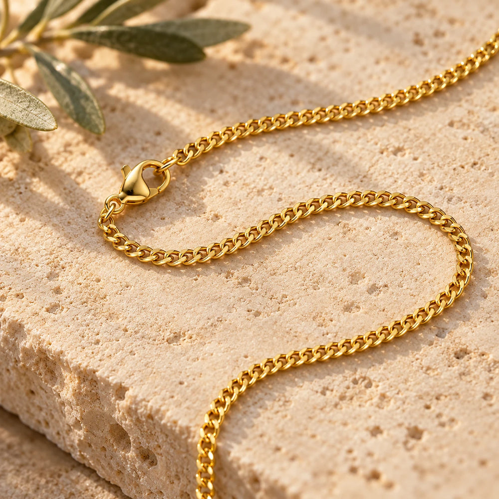 Close-up of the gold-tone 2 mm cuban chain links on limestone beside olive leaves