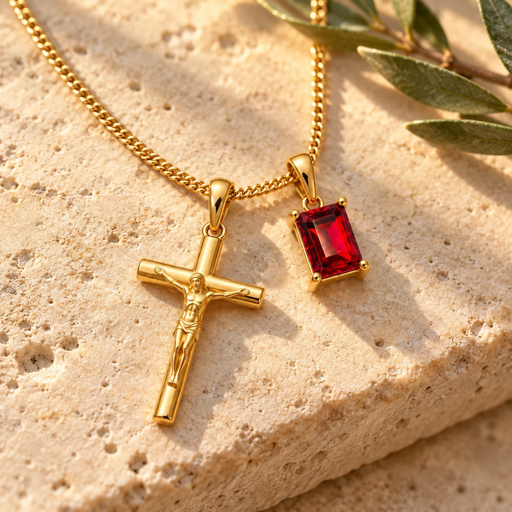 Close-up of the gold-tone crucifix and red stone pendants on limestone beside olive leaves