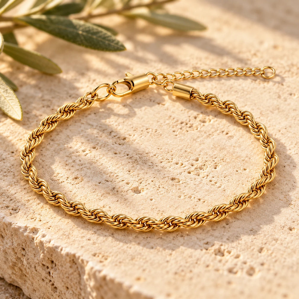 Close-up of the gold-tone 3 mm rope chain bracelet on limestone beside olive leaves