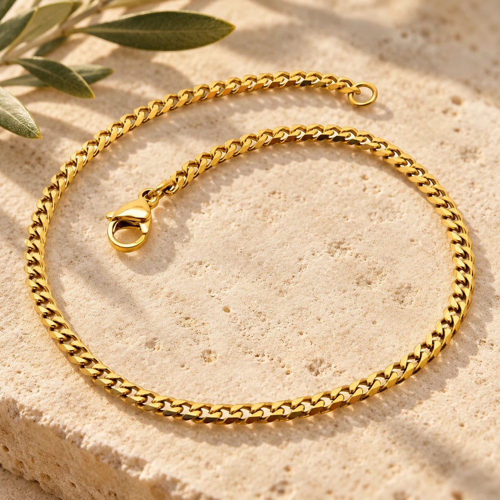 Close-up of the gold-tone 2.5 mm cuban chain bracelet on limestone beside olive leaves