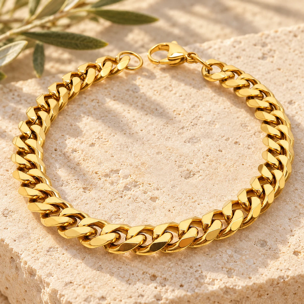 Close-up of the gold-tone 8 mm cuban chain bracelet on limestone beside olive leaves