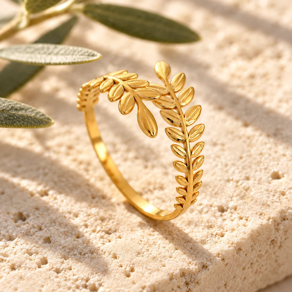 Close-up of the gold-tone olive branch ring on limestone beside olive leaves