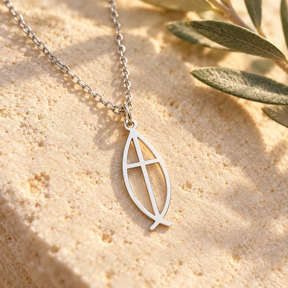 Close-up of the silver-tone ichthys pendant on limestone beside olive leaves