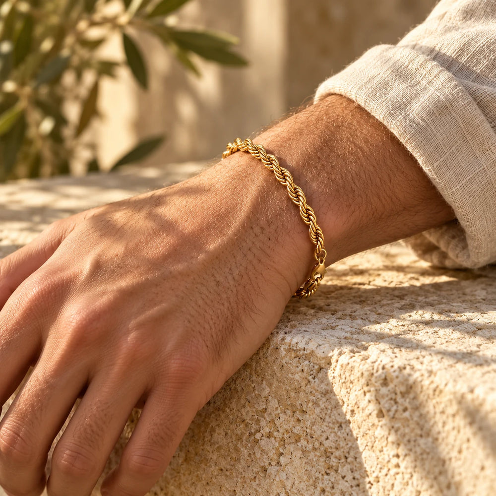 Gold-tone 5 mm rope chain bracelet on a man's wrist resting on a limestone wall — true size: the twisted rope bracelet is 5 mm thick, 21 cm long