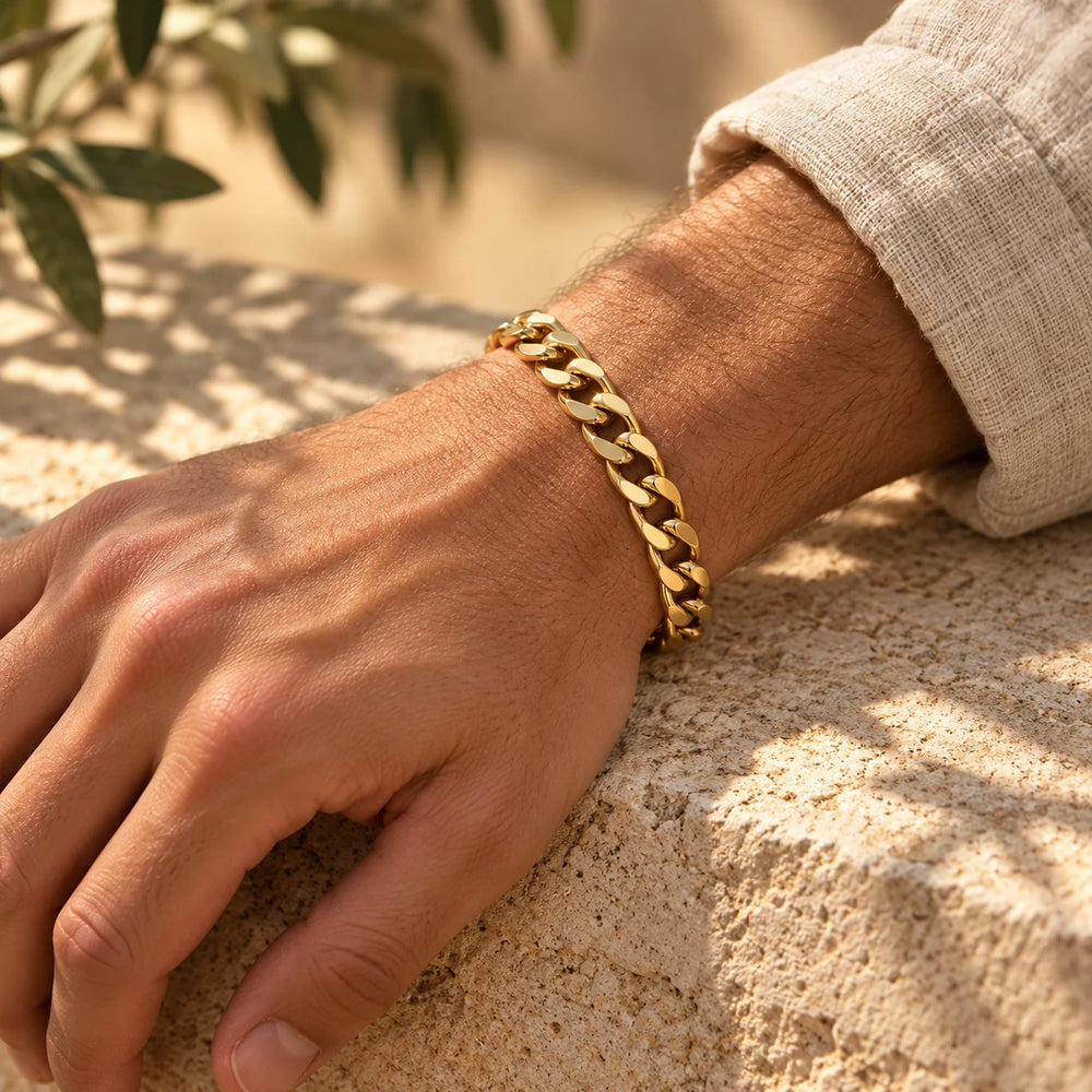 Gold-tone 8 mm cuban chain bracelet on a man's wrist resting on a limestone wall — true size: the flat curb bracelet is 8 mm wide with 2 mm wire, 21 cm long
