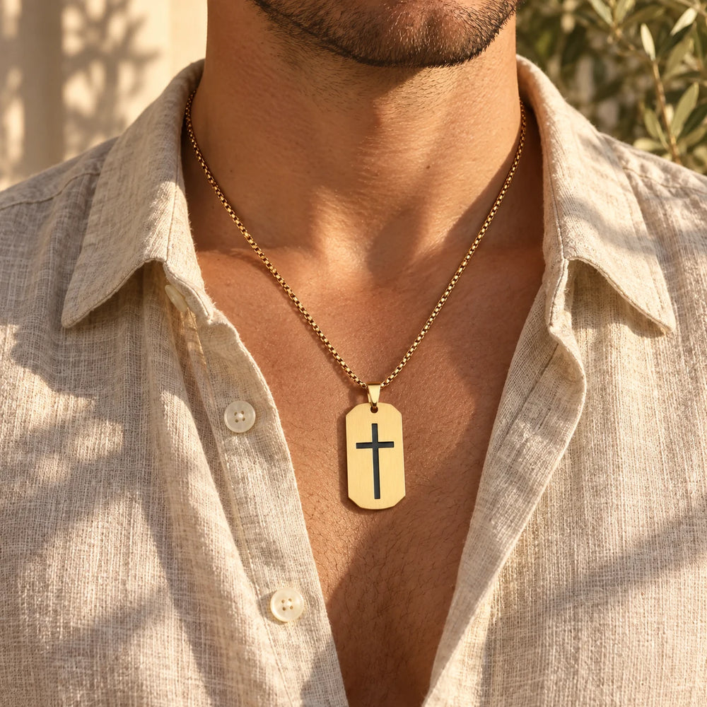 Gold-tone cross tag necklace worn by a man with an open linen shirt