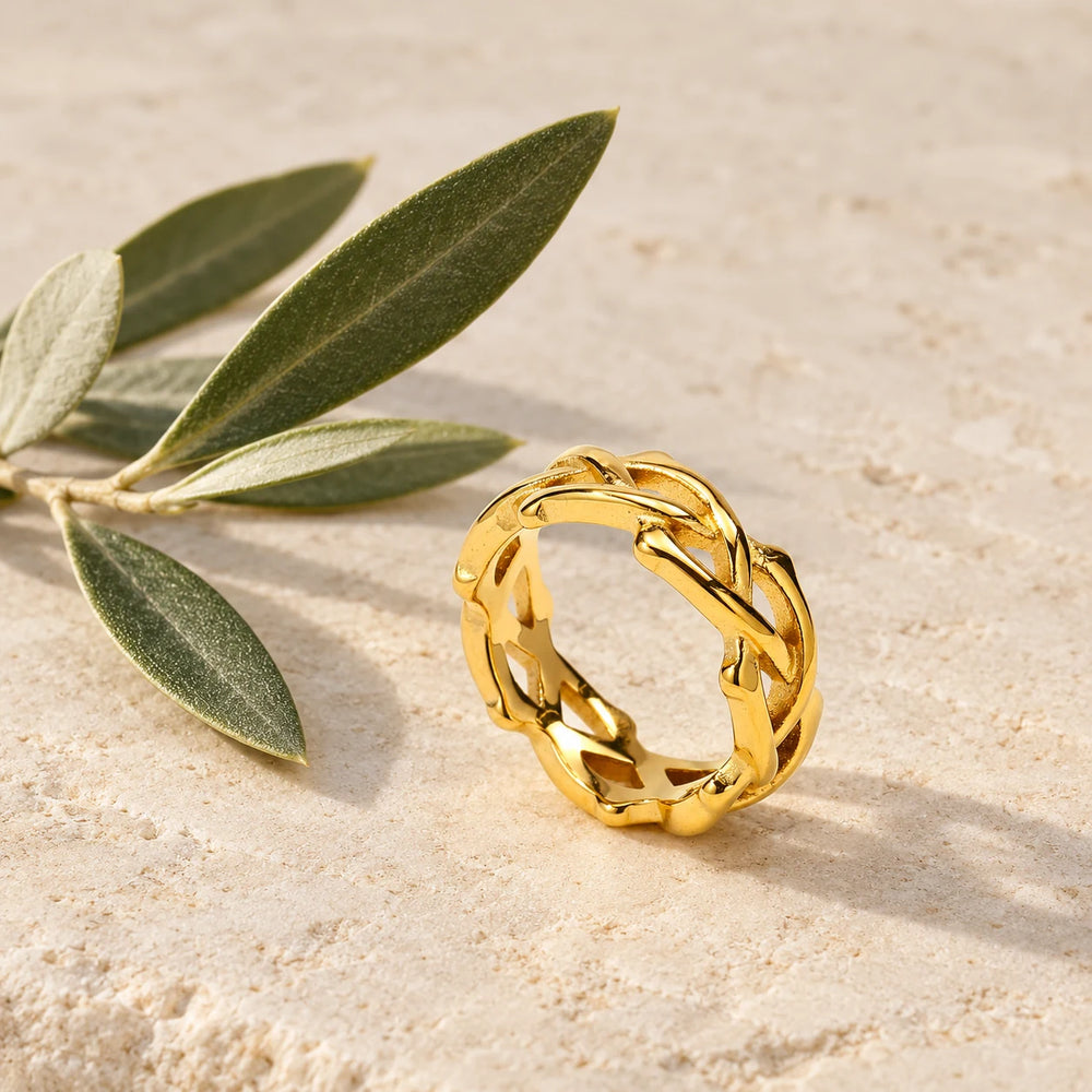 Gold-tone crown of thorns ring of woven vines on a pale limestone background