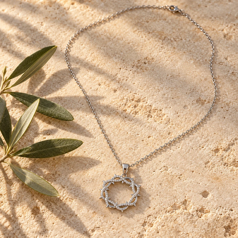 Silver-tone thorn wreath pendant with tiny stones on a fine chain on a pale limestone background, with an olive sprig for scale — true size: the stone-set thorn ring is 22 mm across, about 28 mm tall with its small bail, on a fine cable chain about 1.1 mm thick