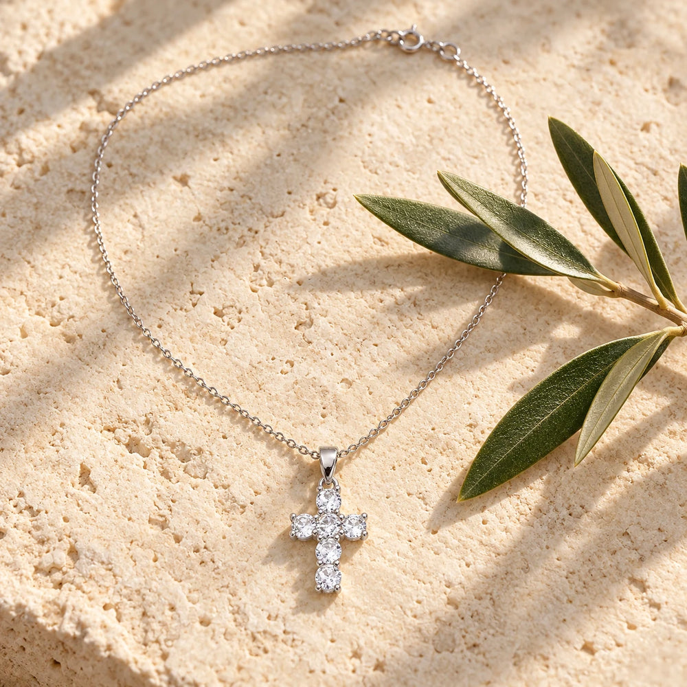 Silver-tone cross with six clear stones on a fine chain on a pale limestone background